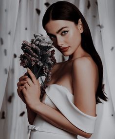 a woman in white dress holding flowers with her right arm around her chest and looking at the camera