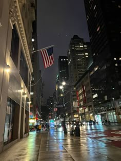 an american flag is flying in the air over a city street with tall buildings at night