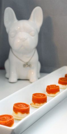 small appetizers are arranged on a long white platter next to a ceramic dog figurine