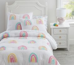 a white bed with rainbows on it in a bedroom next to a night stand