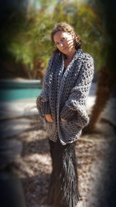 a woman is standing outside wearing a crocheted cardigan