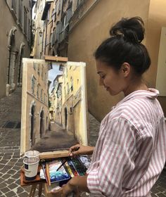 a woman is holding an easel and painting on the street with buildings in the background