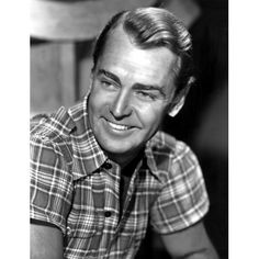 a black and white photo of a man in plaid shirt smiling with his hand on the table