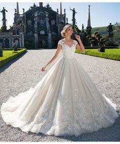 a woman in a wedding dress standing on a gravel road near an ornate building and trees