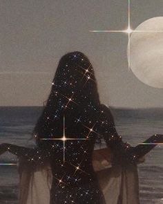 a woman standing in front of the ocean with her back to the camera looking at stars