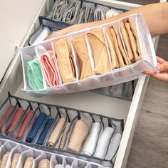 a person is holding an open drawer with several pairs of shoes in it and the bottom section has folded fabric