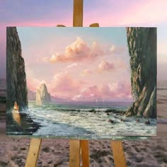 an easel with a painting on it in front of the ocean and cliffs at sunset