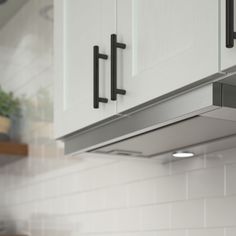 a kitchen with white cupboards and black handles on the wall above it is a potted plant