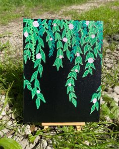 an easel sitting in the grass with green leaves painted on it's side