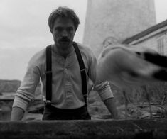 a black and white photo of a man in front of a lighthouse with his hands out