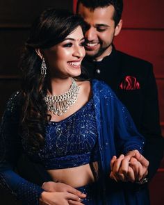 a man standing next to a woman in a blue dress and jewelry on her chest