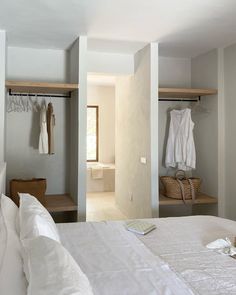 a white bed sitting in a bedroom next to two closets with clothes hanging on hooks