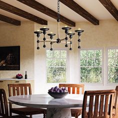 a dining room table with chairs and a bowl of fruit on the table in front of two windows