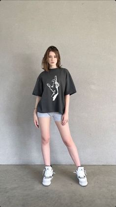 a young woman standing in front of a wall wearing shorts and a t - shirt