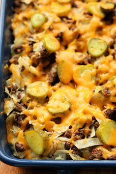 a casserole dish with meat, cheese and cucumbers in it on a wooden table