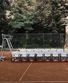 a table set up on a tennis court with white cloths and candles in the middle