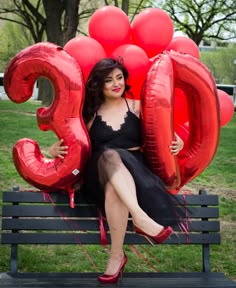 a woman is sitting on a bench with balloons in the shape of numbers