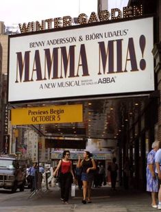 two women walking down the street under a marquee sign for mamma mia