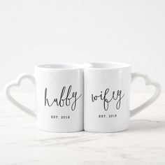 two white coffee mugs with black lettering on them