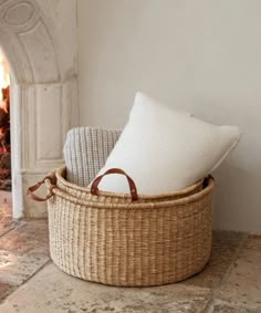 a wicker basket with two pillows in front of a fire place and a fireplace