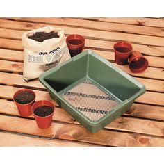 several potted plants sitting on top of a wooden table next to a bag of dirt