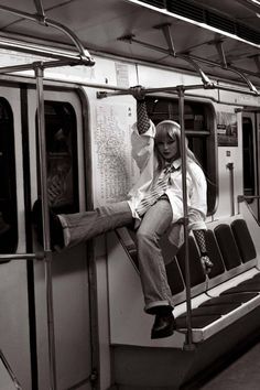 a woman sitting on the side of a subway car with her legs hanging off the rails