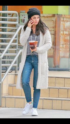 a woman is talking on her cell phone while walking down the street in jeans and a striped shirt