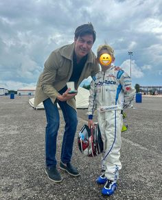 a man standing next to a little boy in a race suit and helmet with an emoticive smiley face painted on his face