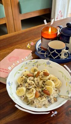 a bowl filled with bananas and nuts on top of a wooden table next to a candle