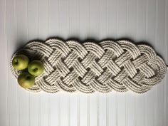 two green apples sitting on top of a rope with knots in the shape of an oar