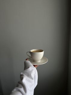 a person is holding a cup and saucer in their hand, against a gray wall