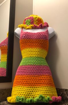 a crocheted dress is displayed in front of a mirror with a hat on it