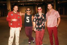 three men standing next to each other in front of a warehouse door wearing red pants and sunglasses