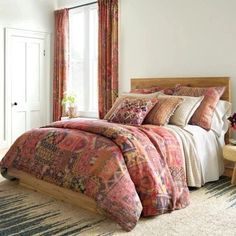 a bed sitting in a bedroom next to a window covered in colorful blankets and pillows