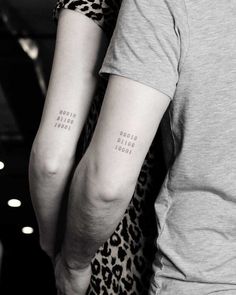 two people with matching tattoos on their arms, one is holding the other's arm