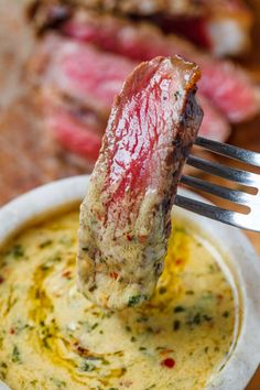 a piece of meat is being lifted from a white bowl with some sauce on it