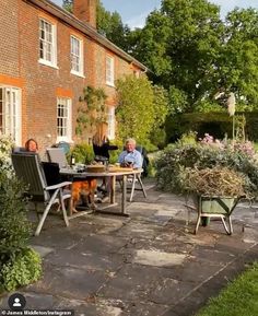 two people sitting at a table outside in front of a brick house with a dog