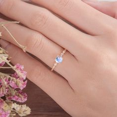 a woman's hand with a ring on her finger and flowers in the background