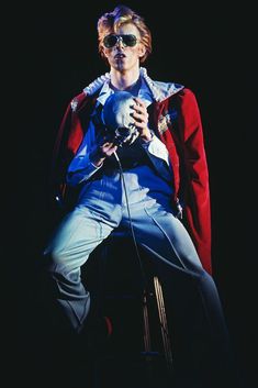 a man sitting on top of a stool wearing sunglasses and holding a microphone in his hand