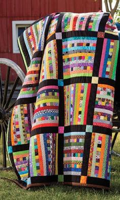 a colorful quilt sitting on top of a grass covered field next to a horse drawn carriage