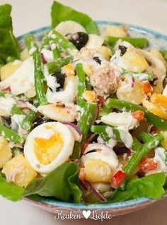 a salad in a bowl with hard boiled eggs and green beans on top, sitting on a table