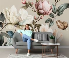 a woman sitting on a couch in front of a floral wall mural