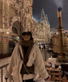 a woman is standing in front of a building with christmas lights on it and snow falling all around her