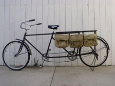 a bicycle with two bags attached to the front rack, parked in front of a white wall