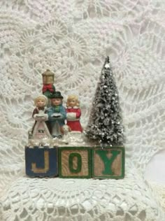 a small christmas tree and two figurines sitting on top of a wooden block