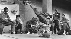 black and white photograph of men doing tricks in front of an adidas building with people watching