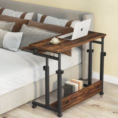 a laptop computer sitting on top of a wooden table next to a bed with pillows