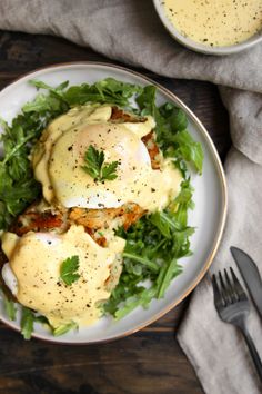 an egg benedict with hollandaise on a white plate next to a fork and knife