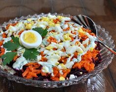 an egg sits on top of a salad in a glass dish with utensils