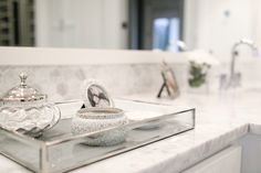 a bathroom counter with a glass tray on top of it that has two dishes and a mirror in front of it